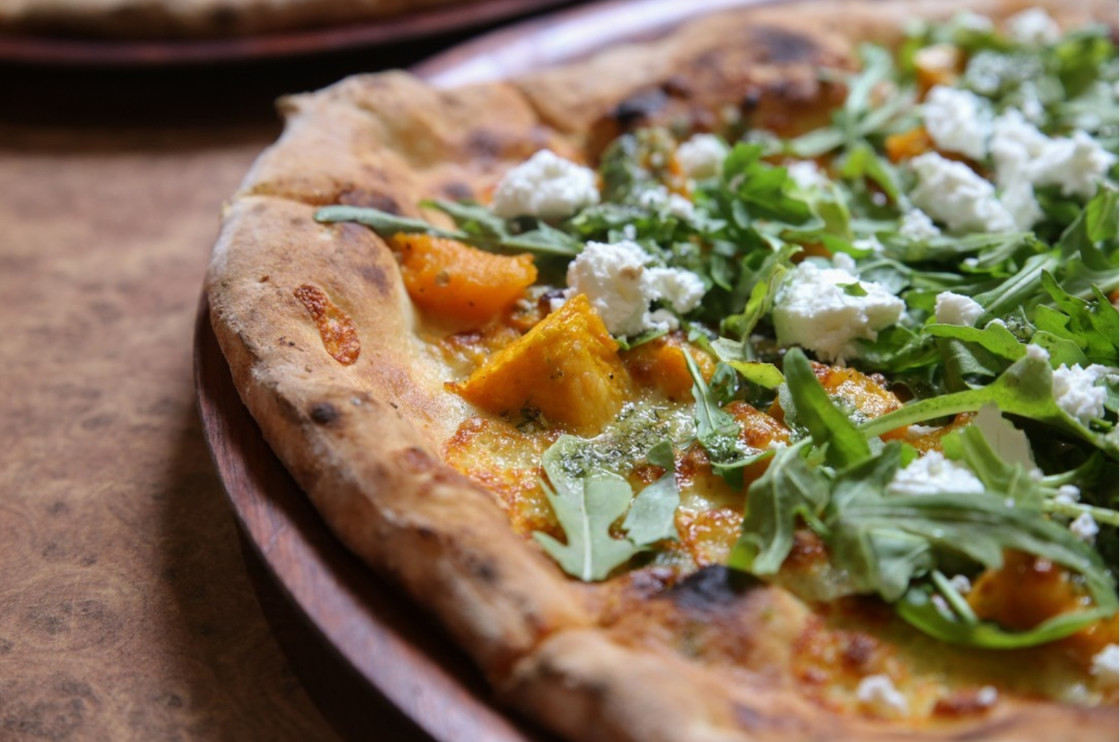 Delicious rustic butternut squash pizza topped with arugula and creamy cheese on a wooden platter.